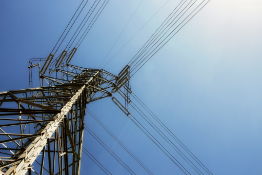 An electrical tower with multiple power lines against a blue sky viewed from the ground up
