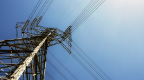 An electrical tower with multiple power lines against a blue sky viewed from the ground up