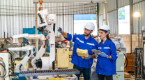 Image of two workers in uniforms in a manufacturing facility working together with machinery in the background.